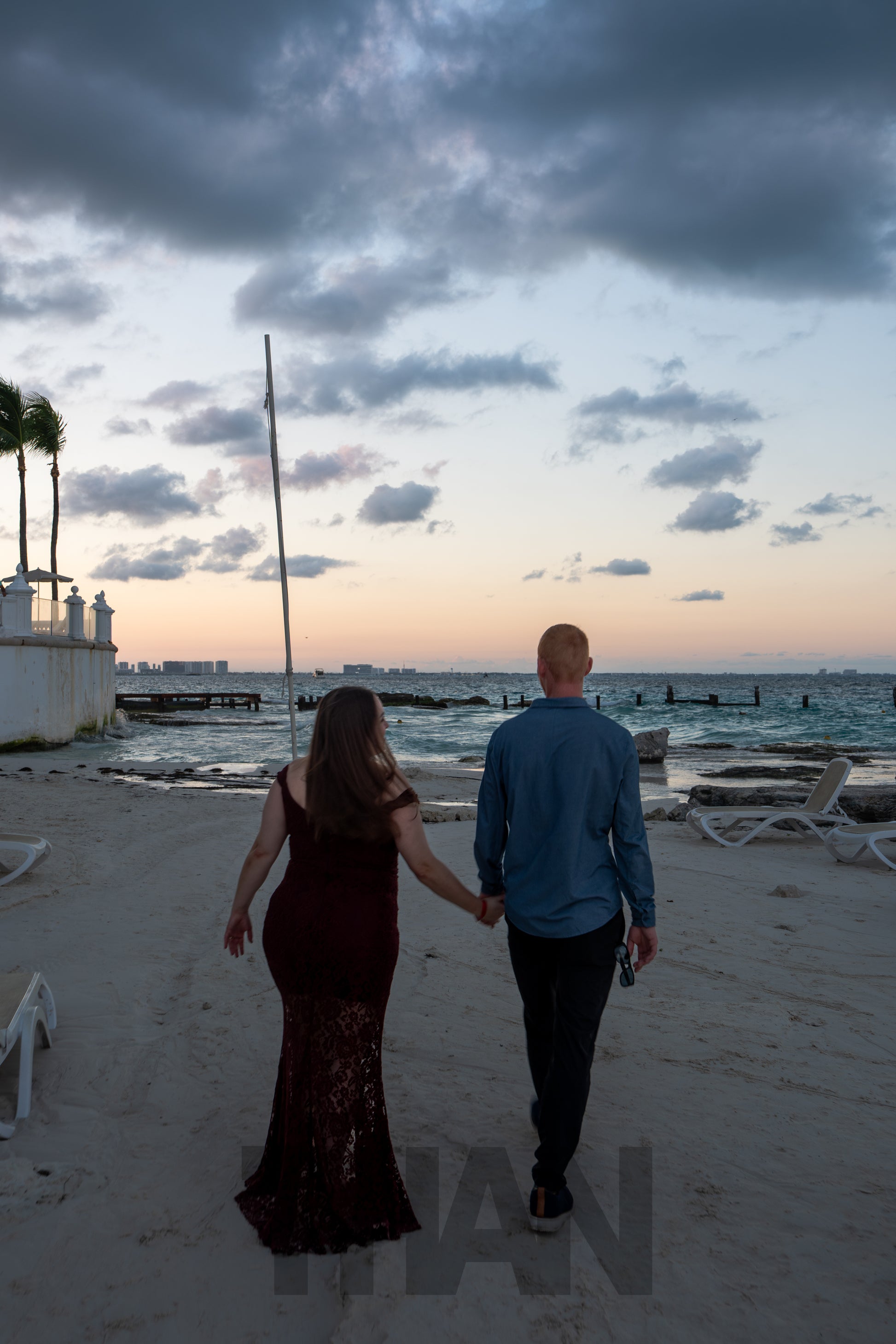 man and woman walking on a beach during a sunset 